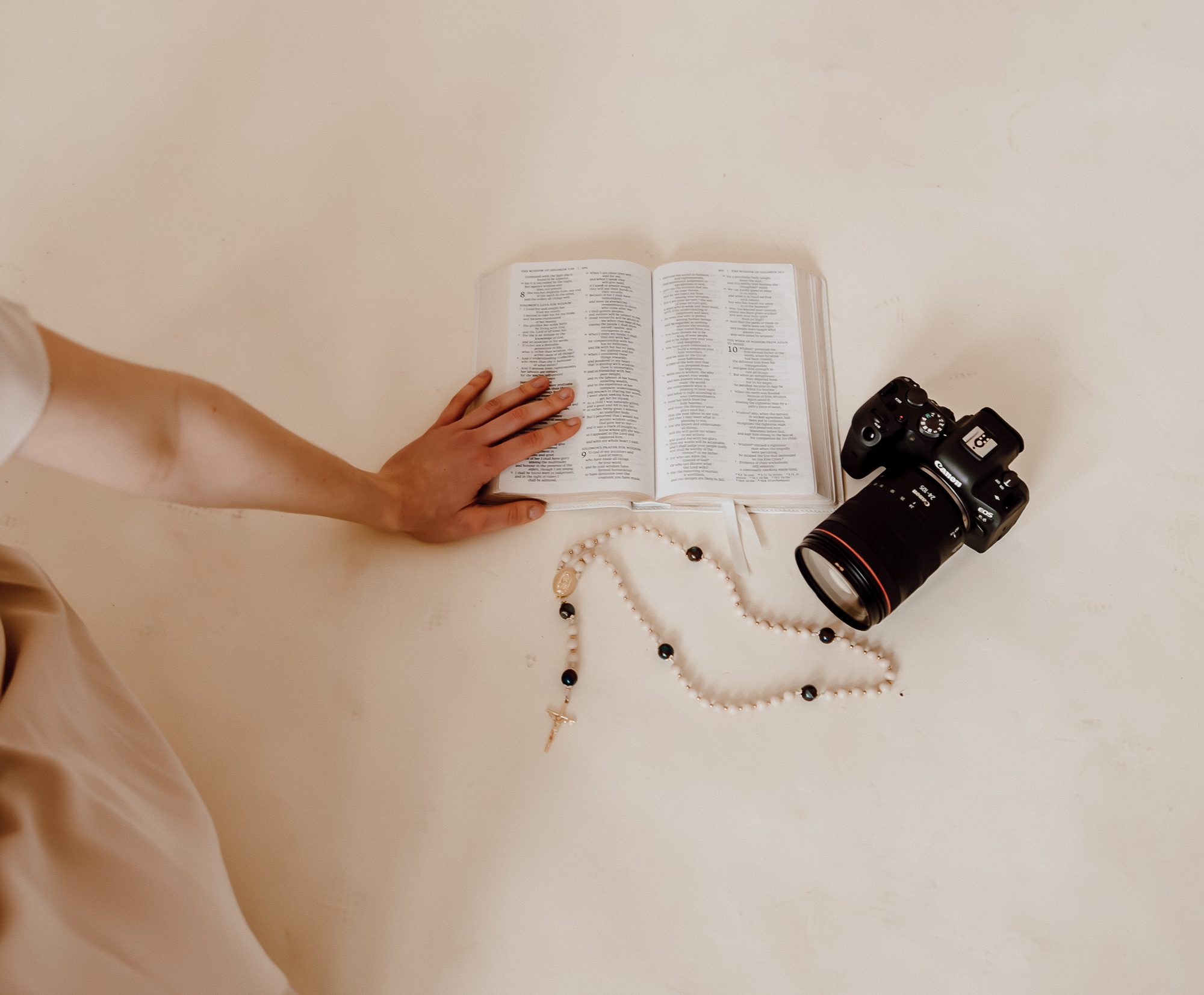An open Bible, a rosary, and a camera resting side by side